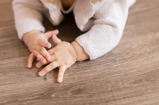Les mains d'un bébé posées sur un parquet.